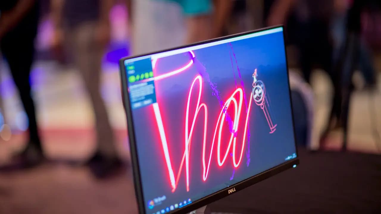 A computer monitor illuminated by vibrant neon lights, showcasing artwork viewed through a VR headset.