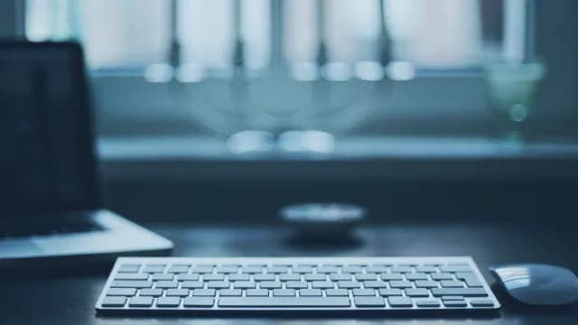 A desk with a keyboard, mouse, and a laptop in soft lighting.